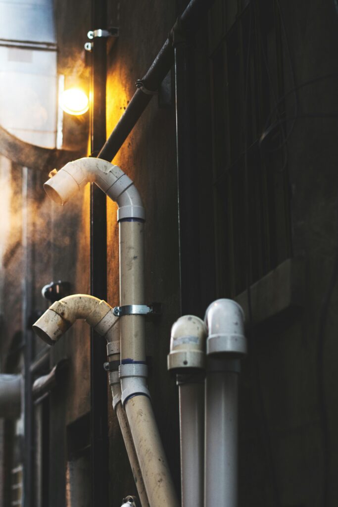 Close-up of industrial pipes with steam and moody lighting outdoors.