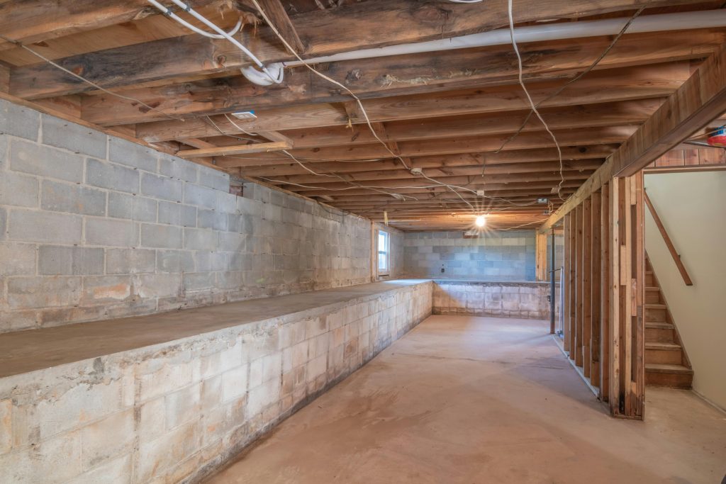 Empty basement with exposed wooden beams, concrete walls and stairs.